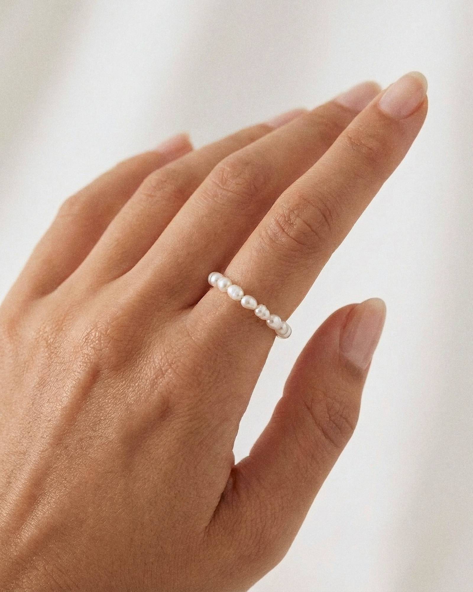 Model wearing a minimalist freshwater pearl ring band on the finger, featuring small natural white pearls arranged in a delicate row. Designed for women seeking a lightweight, elegant pearl ring for everyday wear that offers a refined, comfortable alternative to traditional metal rings.
