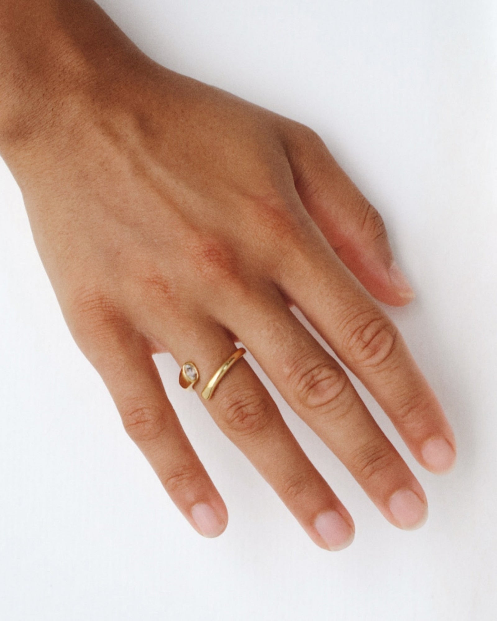 Close-up of a hand wearing the Celine gold open ring with a white cubic zirconia stone on a minimal white background. Designed for women who want an elegant everyday ring, this stainless steel ring with 18k gold PVD adds subtle sparkle and helps elevate simple outfits with minimal effort.