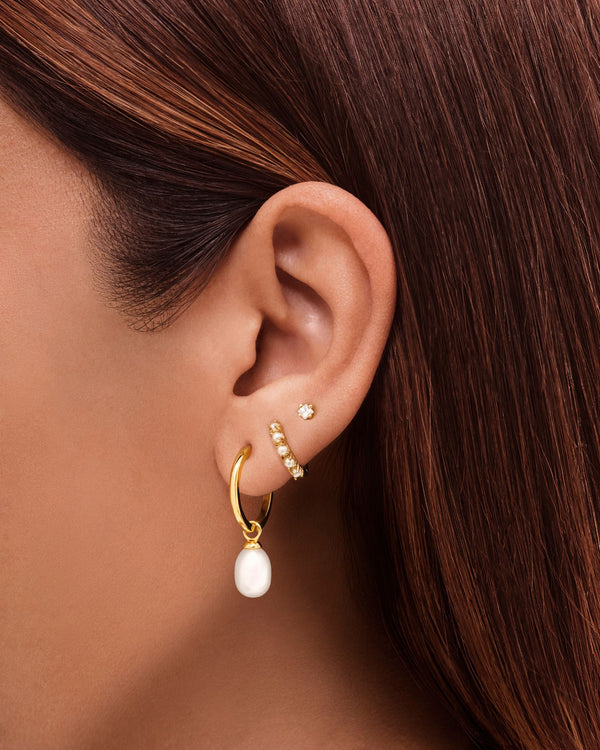 Close-up side profile of a woman wearing gold pearl hoop earrings with a single dangling freshwater pearl, paired with a slim crystal-studded ear cuff and a small gold stud in the upper lobe. Designed for women who prefer minimalist gold jewellery and refined ear stacking, this image demonstrates how pearl hoop earrings can be styled for everyday elegance, bridal looks, and special occasions. Ideal for those seeking lightweight, versatile pearl earrings 