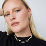 Close-up portrait of a model wearing a short freshwater pearl necklace layered with a fine gold chain and small gold hoop earrings. Designed for women seeking a refined pearl necklace that sits close to the neck, ideal for minimalist styling, everyday wear, and effortless layering with gold jewellery for a polished, modern look.