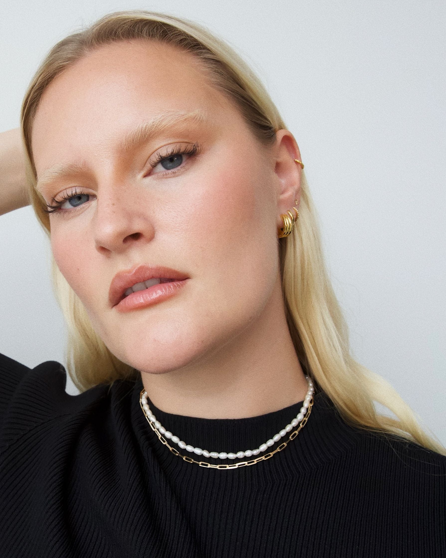 Close-up portrait of a model wearing a short freshwater pearl necklace layered with a fine gold chain and small gold hoop earrings. Designed for women seeking a refined pearl necklace that sits close to the neck, ideal for minimalist styling, everyday wear, and effortless layering with gold jewellery for a polished, modern look.
