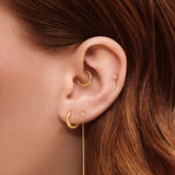 Close-up of a model’s ear styled with layered gold jewellery, featuring a small gold hoop earring, a textured gold ear cuff, delicate gold stud earrings, and a fine chain drop earring. Designed for women seeking curated ear styling inspiration and versatile everyday gold earrings that can be mixed and layered for a minimalist, modern look.