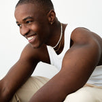 Lifestyle image of a male model wearing a short freshwater pearl necklace layered with a fine gold chain and a small gold hoop earring, styled with a white tank top. Designed for men seeking a modern pearl necklace that offers a relaxed, gender-neutral approach to jewellery, ideal for everyday wear, layering, and adding understated elegance to casual outfits.