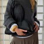 Woman wearing the Lumi butter yellow resin bangle with a grey oversized cashmere sweater, black leather shoulder bag, and neutral skirt. A chunky glossy resin bracelet styled for minimal everyday outfits, capsule wardrobes, Scandinavian fashion, and elevated essentials.