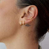 Side profile close-up of a woman’s ear styled with a layered gold ear stack, featuring two slim no-piercing ear cuffs on the upper ear and two small gold hoop earrings in the lobe, one accented with clear gemstones. The image highlights minimalist gold ear jewellery designed for people who want a curated, stacked ear look without additional piercings, offering an easy way to add subtle sparkle, balance, and everyday elegance to an ear stack.