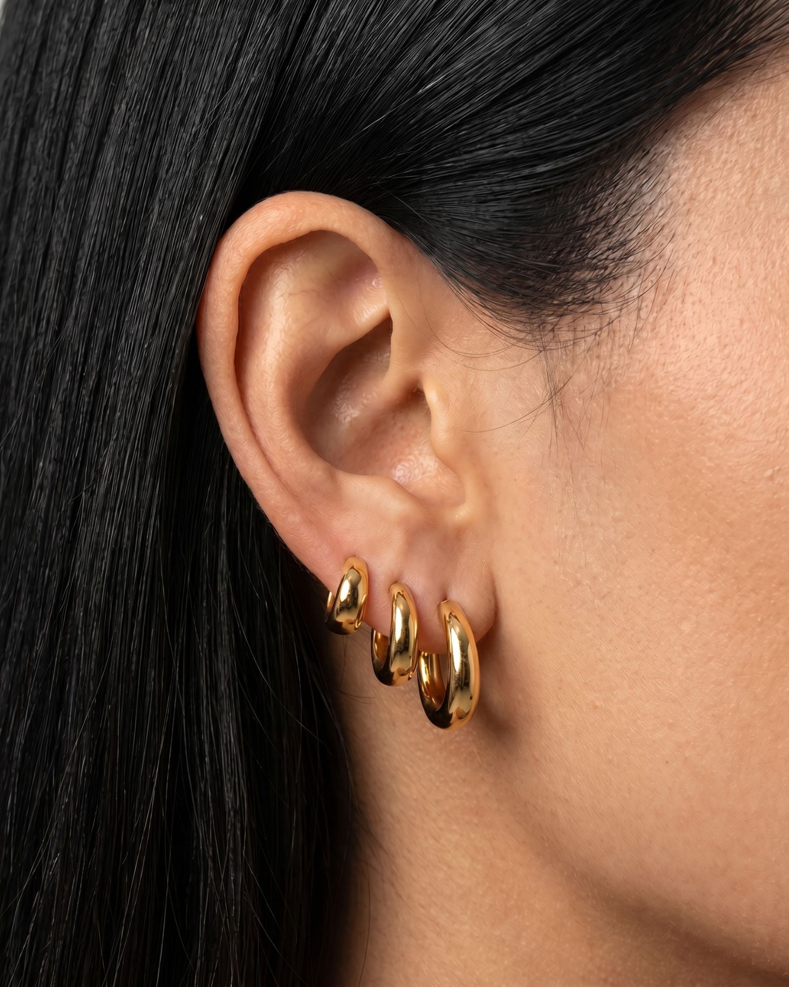 Model wearing SELENE rounded gold hoop earrings in small, medium and large sizes. Polished sterling silver hoops with micron 18k gold plating styled as a layered ear stack for timeless everyday jewellery looks and elevated minimal styling.