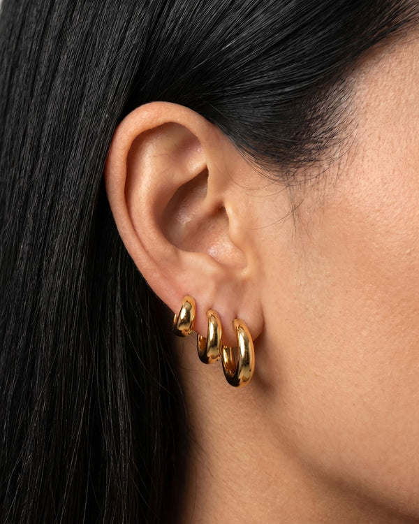 Model wearing SELENE rounded gold hoop earrings in small, medium and large sizes. Polished sterling silver hoops with micron 18k gold plating styled as a layered ear stack for timeless everyday jewellery looks and elevated minimal styling.