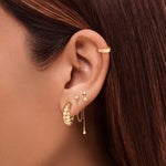 Close-up of a woman’s ear styled with layered gold earrings, featuring twisted gold hoop earrings, delicate gold chain drop studs, and a minimalist gold ear cuff. Designed for women seeking everyday gold earrings and modern ear stacking inspiration, this image shows how small gold hoops and dainty drop earrings can be layered to create a polished, versatile look for multiple piercings and effortless daily wear.