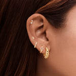 Close-up of a woman’s ear styled with layered gold earrings, including a small twisted gold hoop, pavé huggie, star-shaped stud, and minimalist gold cartilage studs. Designed for women looking for everyday gold earrings and curated ear styling ideas, showing how small gold hoops and studs can be layered for a modern, polished look that works for multiple piercings and effortless daily wear.