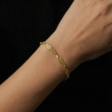 Close-up of a woman’s wrist wearing a slim gold bracelet with textured, organically shaped links, photographed against a dark background. The image clearly shows the bracelet’s warm gold tone, detailed surface finish, and how it sits naturally on the wrist. Designed for women seeking refined, everyday gold bracelets that add subtle interest without overpowering an outfit, this image helps customers understand scale, fit, and how a delicate gold bracelet elevates a minimal, modern look.
