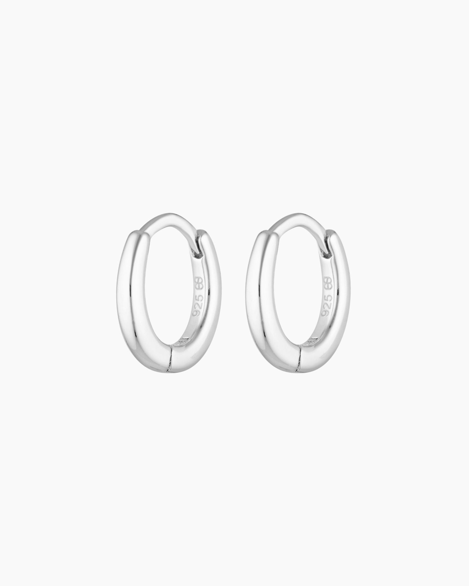 Pair of polished silver oval huggie hoop earrings shown on a clean white background, featuring a smooth, rounded silhouette and a secure hinged clasp with a 925 sterling silver stamp. Designed for women seeking minimalist silver hoop earrings for everyday wear, these lightweight huggie hoops suit sensitive ears and offer a comfortable, tarnish-resistant option for daily styling, stacking with other earrings, or wearing alone for a clean, modern look.