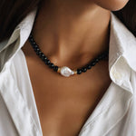 model wearing a black beaded necklace with onyx, gold details and white natural baroque pearl in the middle 
