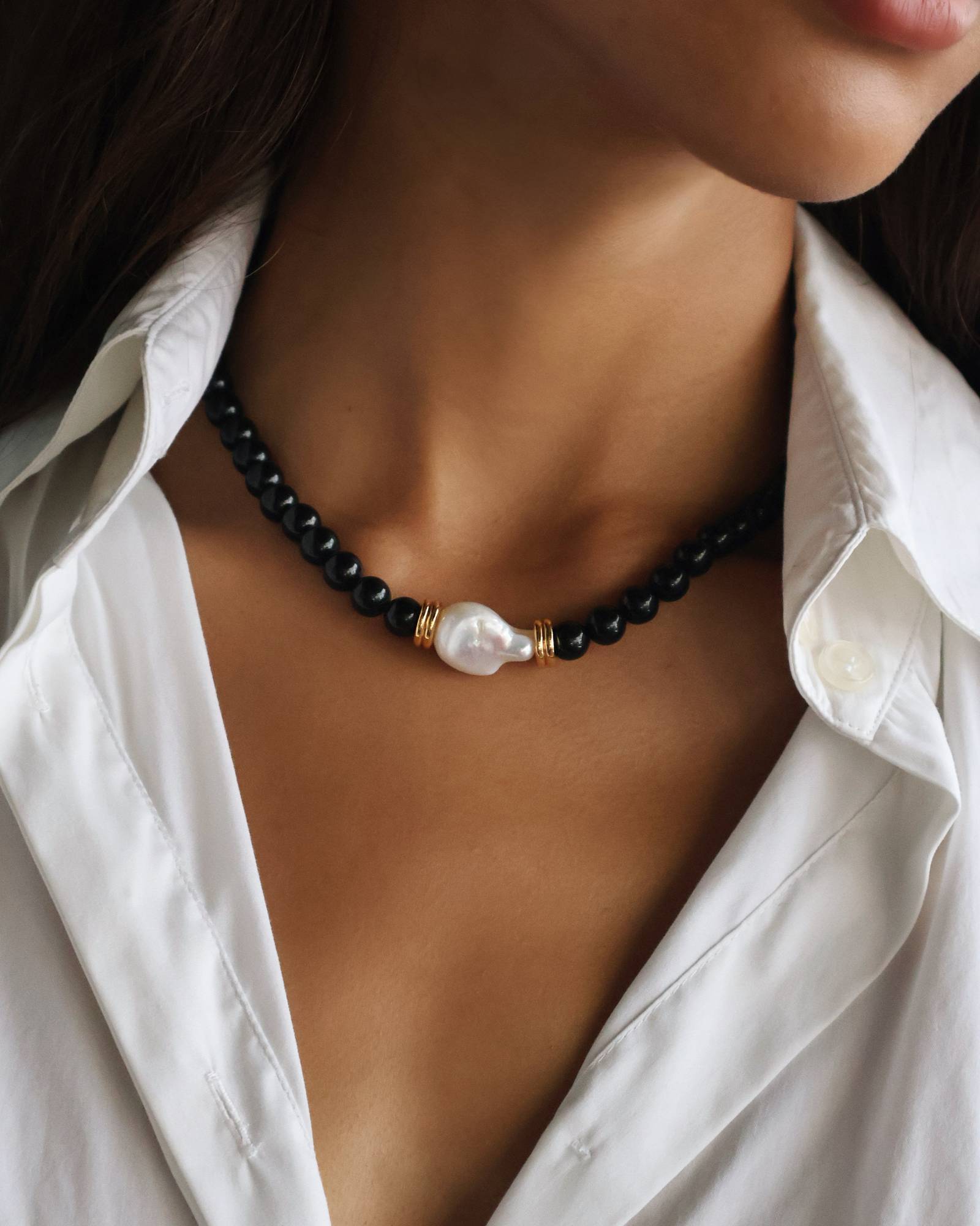 model wearing a black beaded necklace with onyx, gold details and white natural baroque pearl in the middle 