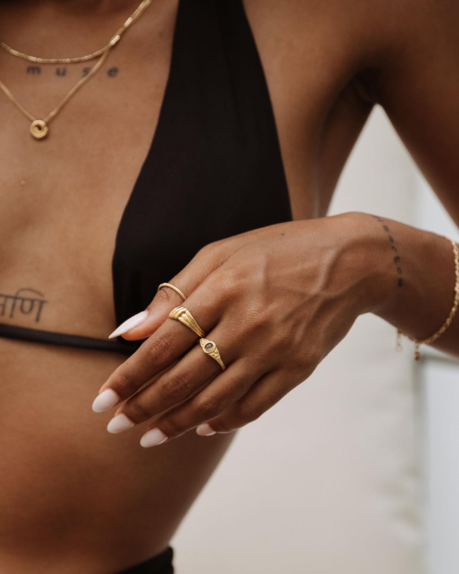 Lifestyle image of a woman wearing a vintage-inspired gold ring with a soft twisted design, stacked with a slim gold band and a signet-style gold ring, paired with layered gold necklaces. Designed for women seeking everyday gold rings for stacking, this image shows how minimalist gold jewellery creates an effortless, cohesive look while solving the need for versatile pieces that transition from casual wear to elevated styling.