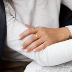 Lifestyle image of a woman wearing a vintage-inspired gold ring with a soft twisted design, stacked with a textured gold band, shown while seated in a relaxed setting. Intended for women looking for everyday gold rings for stacking, this image demonstrates how minimalist gold jewellery offers a comfortable, low-maintenance solution for polished daily wear.
