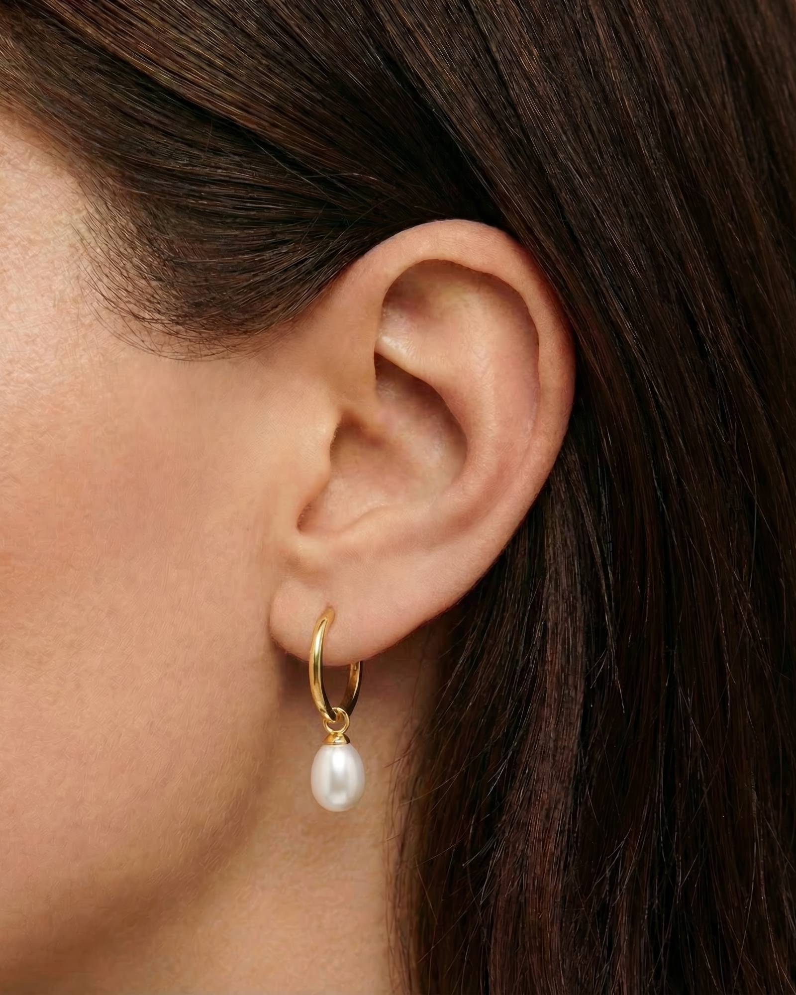 Close-up side view of a model wearing small gold pearl hoop earrings, featuring a dainty 18K gold–plated hoop with a single white freshwater pearl drop. Designed for women seeking minimalist pearl jewellery, these lightweight hoop earrings offer an elegant solution for everyday wear, bridal styling, or refined occasions, adding softness and movement without overpowering the ear. Ideal for those wanting timeless gold earrings that elevate simple outfits while remaining comfortable and versatile.