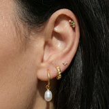 Curated ear stack featuring a gold flat back cartilage stud with a green pear-cut gemstone, paired with gold pearl drop earrings and minimalist studs for a layered look.