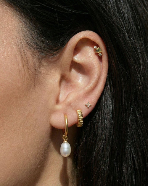 Curated ear stack featuring a gold flat back cartilage stud with a green pear-cut gemstone, paired with gold pearl drop earrings and minimalist studs for a layered look.