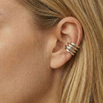 Close-up side profile of a woman wearing a polished silver ear cuff with a stacked, multi-band design wrapped around the outer ear cartilage, worn without a piercing. The photo highlights the smooth silver finish, layered structure, and secure fit against natural skin and blonde hair. Designed for women seeking a modern, no-piercing silver ear cuff, this image helps customers visualise scale, placement, and how a statement ear cuff elevates a clean, contemporary style.