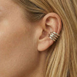 Close-up side profile of a woman wearing a polished silver ear cuff with a stacked, multi-band design wrapped around the outer ear cartilage, worn without a piercing. The photo highlights the smooth silver finish, layered structure, and secure fit against natural skin and blonde hair. Designed for women seeking a modern, no-piercing silver ear cuff, this image helps customers visualise scale, placement, and how a statement ear cuff elevates a clean, contemporary style.