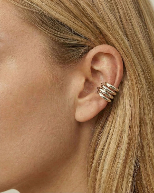 Close-up side profile of a woman wearing a polished silver ear cuff with a stacked, multi-band design wrapped around the outer ear cartilage, worn without a piercing. The photo highlights the smooth silver finish, layered structure, and secure fit against natural skin and blonde hair. Designed for women seeking a modern, no-piercing silver ear cuff, this image helps customers visualise scale, placement, and how a statement ear cuff elevates a clean, contemporary style.