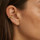 Close-up side profile of a woman wearing a polished gold ear cuff with a smooth, double-band design, positioned on the outer ear cartilage without a piercing. The image clearly shows the cuff’s rounded shape, warm gold tone, and snug fit against natural skin and brown hair. Designed for women who want an easy, non-pierced ear accessory, this image helps customers understand how a minimalist gold ear cuff sits on the ear and adds subtle definition to an everyday look.