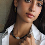 model wearing wavy thread earrings with a black beaded onyx necklace with gold details and a white natural baroque pearl