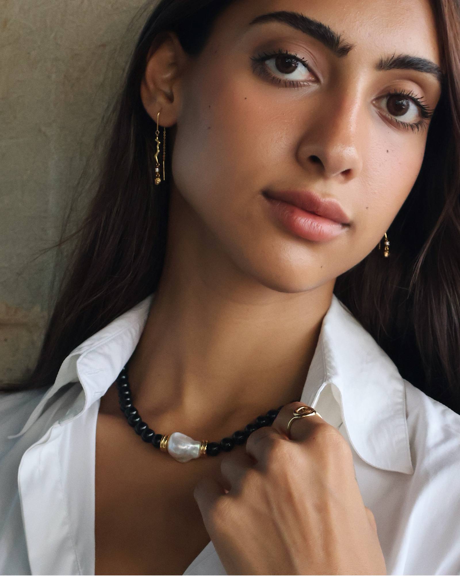 model wearing wavy thread earrings with a black beaded onyx necklace with gold details and a white natural baroque pearl