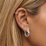 ear stack with wavy textured silver hoop in  the cartilage with a dainty small square cubic zirconia stone in white and silver, dangly freshwater pearl with a small square cubic zirconia stone, classic unisex silver hoop and a euro summer inspired medium sized silver hoops with blue, white and light yellow gemstones.  