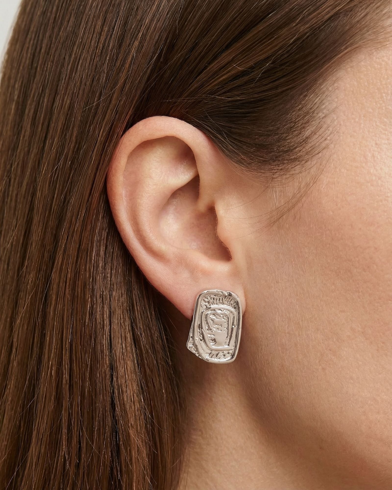 Close-up side profile of a woman’s ear wearing a silver statement stud earring with an organic, sculptural rectangular shape and textured surface. Designed for women who want bold yet refined silver jewellery, this image helps customers understand the size, shape, and fit of the silver stud earring for everyday wear or minimalist statement styling.