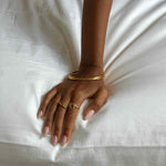 Product image of a woman’s hand resting on white fabric, wearing an organic spiral gold ring paired with a slim gold band and gold bangles. Designed for women seeking minimalist gold jewellery for everyday wear, this image highlights how a spiral gold stacking ring creates a refined, effortless look while remaining comfortable and easy to style daily.