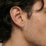 Close-up side profile of a person wearing a small polished silver hoop earring in a pierced earlobe. The minimalist hoop sits snugly against the ear with a smooth, rounded finish, shown against natural skin texture and short facial hair. This image is for customers looking for a simple, everyday silver hoop earring that is lightweight, understated, and suitable for daily wear or layering with other jewellery.