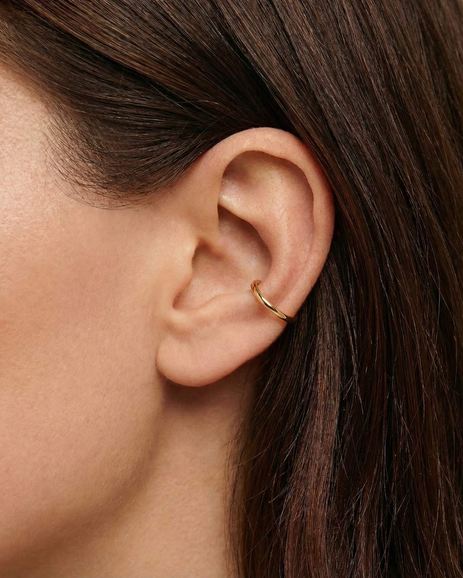 Minimalist gold ear cuff worn on the cartilage of a woman’s ear, shown in a close-up side profile with smooth polished finish. Designed for women who want a clean, modern ear stack without a piercing, this no-piercing ear cuff offers an easy way to add subtle gold jewellery to everyday looks while remaining lightweight, comfortable, and suitable for sensitive skin.