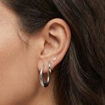 Close-up side profile of a woman’s ear wearing polished silver hoop earrings in two sizes, paired with a small silver marquise-shaped stud in the upper lobe. The image highlights the smooth, reflective finish and classic rounded shape of the silver hoops against natural skin and dark hair. Designed for women who want versatile, everyday silver earrings that are easy to style and suitable for multiple piercings, this image helps shoppers visualise scale, layering, and how minimal silver hoops look when worn.