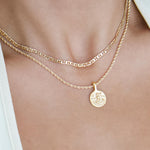 Layered gold necklaces worn on the neck, featuring a slim flat-link gold chain paired with a rope chain and a round gold coin pendant. Styled for women seeking minimalist gold necklaces for everyday wear and layering, offering an effortless solution for building a refined, versatile jewellery stack that elevates simple outfits.