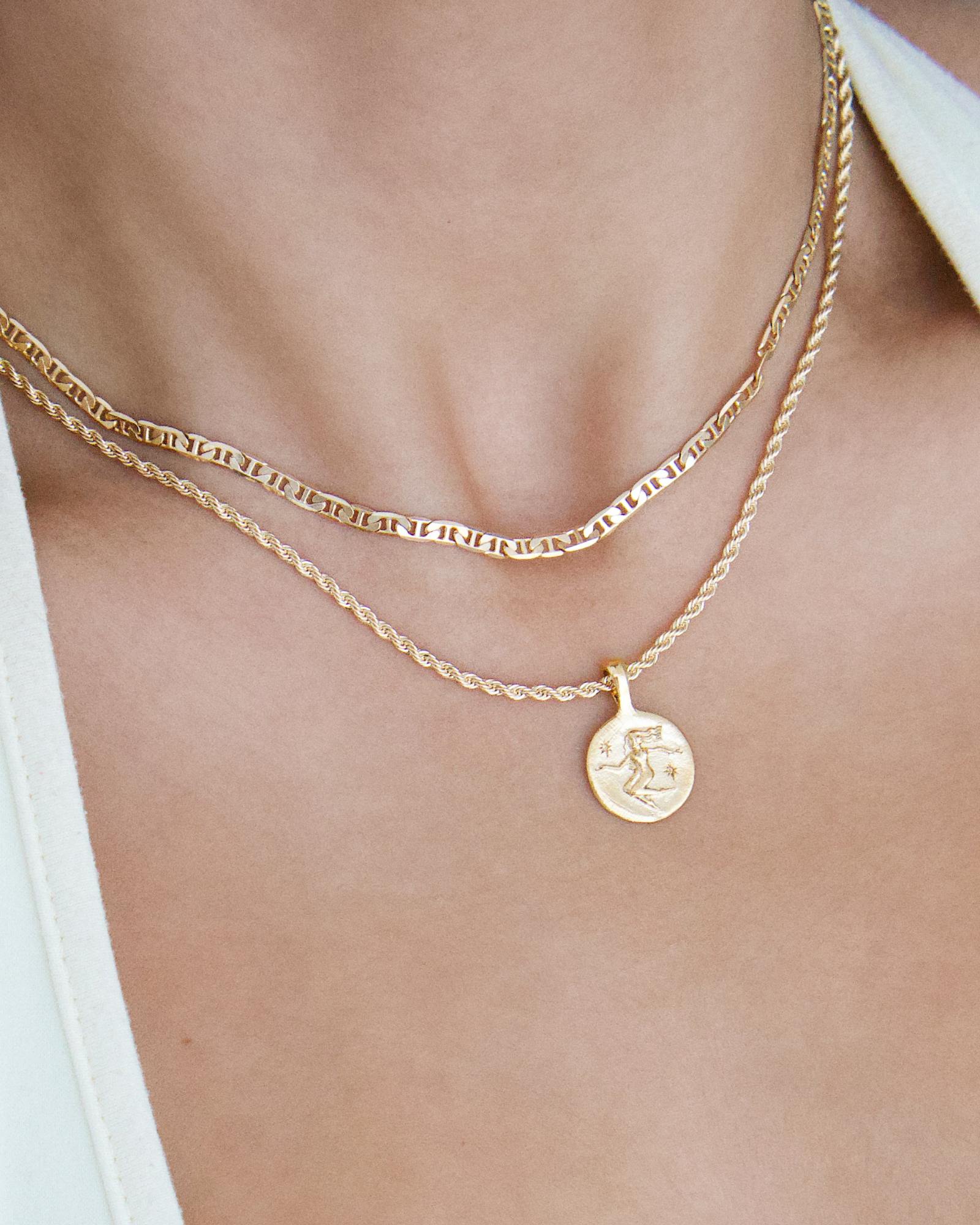 Layered gold necklaces worn on the neck, featuring a slim flat-link gold chain paired with a rope chain and a round gold coin pendant. Styled for women seeking minimalist gold necklaces for everyday wear and layering, offering an effortless solution for building a refined, versatile jewellery stack that elevates simple outfits.