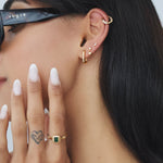 Side profile of a woman wearing a rectangular green emerald cubic zirconia gold ring on her finger, paired with layered gold hoop and stud earrings and a gold ear cuff. Styled for women seeking modern, vintage-inspired gold jewellery that adds colour and interest to everyday outfits while remaining minimal, wearable, and easy to layer.