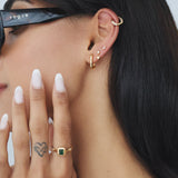 Side profile of a woman wearing a rectangular green emerald cubic zirconia gold ring on her finger, paired with layered gold hoop and stud earrings and a gold ear cuff. Styled for women seeking modern, vintage-inspired gold jewellery that adds colour and interest to everyday outfits while remaining minimal, wearable, and easy to layer.