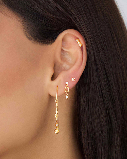 Layered ear stack featuring a gold freshwater pearl drop earring with oval link, long gold drop earring, and multiple zirconia studs for a modern gold jewellery look.