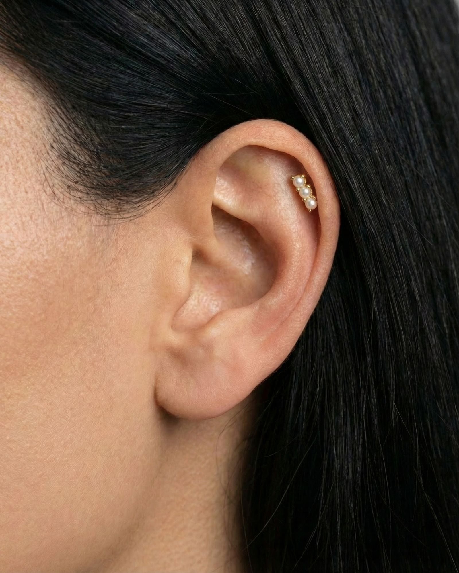 Close-up of a gold flat back cartilage stud featuring three petite freshwater pearls set in a vertical row, worn in the upper ear helix. Designed for women seeking comfortable flat back ear piercings for sensitive ears, this minimalist pearl stud offers a secure, low-profile option for healed or new cartilage piercings, suitable for everyday wear, bridal styling, and all-day comfort.