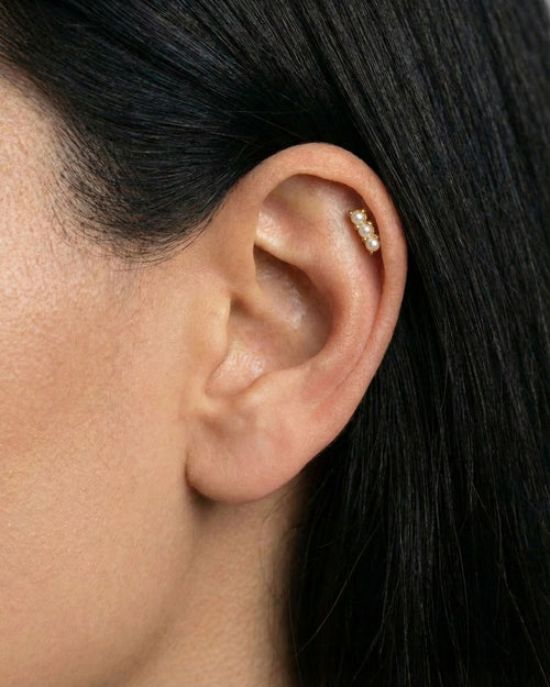 Close-up of a gold flat back cartilage stud featuring three petite freshwater pearls set in a vertical row, worn in the upper ear helix. Designed for women seeking comfortable flat back ear piercings for sensitive ears, this minimalist pearl stud offers a secure, low-profile option for healed or new cartilage piercings, suitable for everyday wear, bridal styling, and all-day comfort.