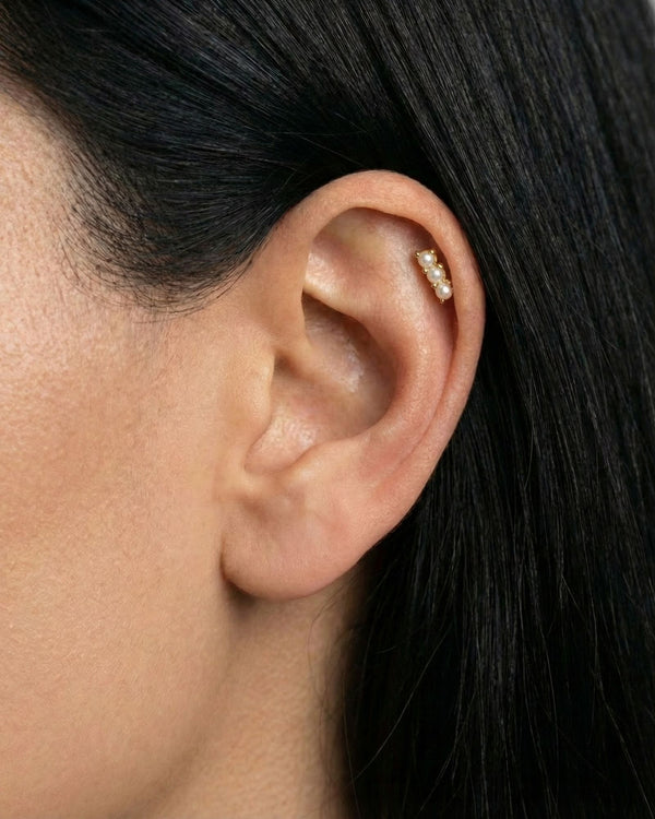 Close-up of a gold flat back cartilage stud featuring three petite freshwater pearls set in a vertical row, worn in the upper ear helix. Designed for women seeking comfortable flat back ear piercings for sensitive ears, this minimalist pearl stud offers a secure, low-profile option for healed or new cartilage piercings, suitable for everyday wear, bridal styling, and all-day comfort.