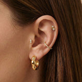 Close-up of a woman’s ear wearing Bella gold hoop earrings paired with a slim textured gold ear cuff and small crystal studs placed across the lobe and cartilage. This image is for women looking for gold hoop earrings that anchor a refined ear stack and show how to balance hoops, cuffs, and delicate studs for a cohesive everyday jewellery look.