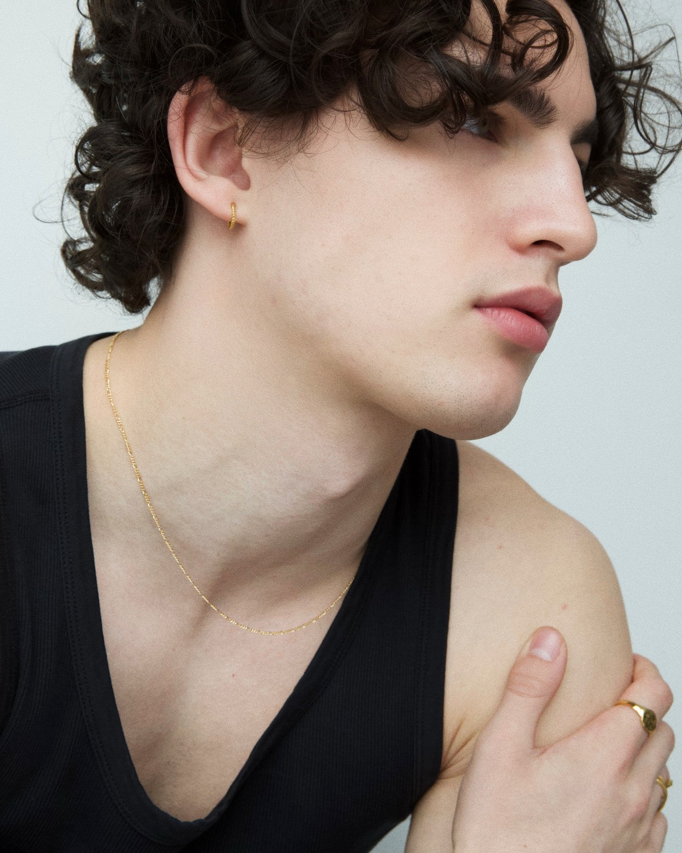 Side-profile close-up of a model wearing a fine 18K gold-filled chain necklace and a small gold hoop earring, styled with a black sleeveless top and gold rings. This image is for women and men looking for minimalist gold jewellery, showcasing a lightweight everyday gold necklace that sits neatly on the collarbone and solves the need for a subtle, versatile chain suitable for daily wear, layering, and a clean modern look.