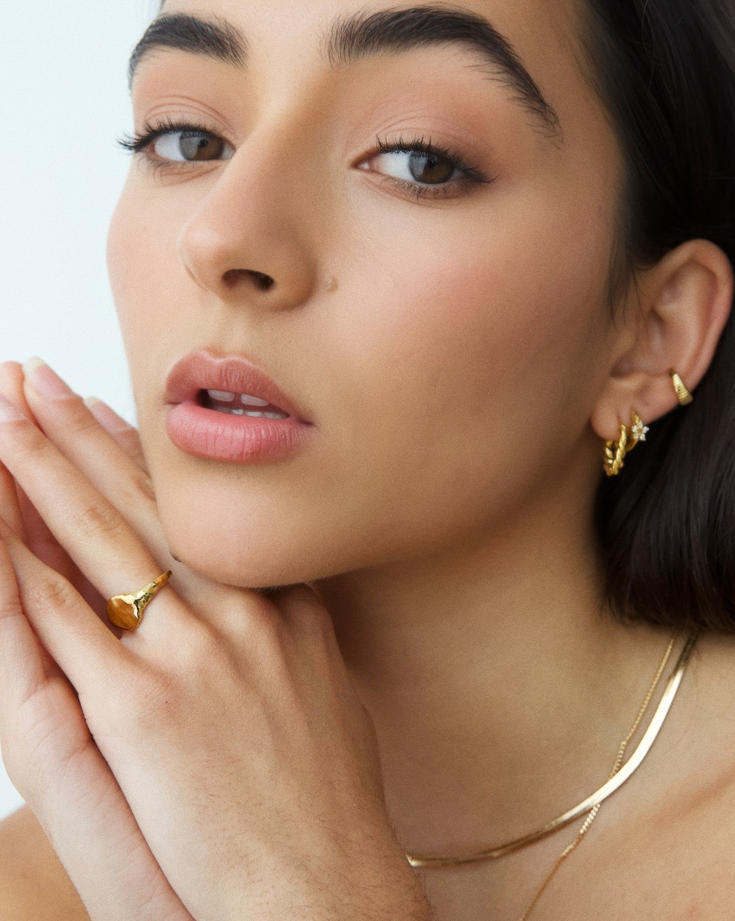 Product image showing a model wearing a flat organic gold signet ring paired with small gold hoop earrings and layered gold necklaces. Designed for those searching for modern gold signet rings, minimalist gold jewelry, and everyday luxury accessories, this image highlights a sculptural gold ring that offers a refined alternative to traditional signet rings. Ideal for customers looking for durable, water-safe gold rings that elevate daily wear with a clean, contemporary aesthetic.