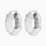Silver statement hoop earrings with bold sculptural layered texture, rhodium plated design photographed on a white background.