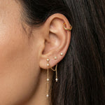 Close-up side profile of a woman’s ear wearing a layered gold ear stack, featuring a textured gold ear cuff on the upper cartilage, delicate gold stud earrings, and a fine gold chain drop earring accented with small pearls. The image clearly shows the soft movement of the chain, the contrast between polished gold and pearl details, and the placement across multiple piercings. Designed for women who enjoy elegant, feminine ear styling, this image helps customers visualise how to combine gold studs, cuffs, an