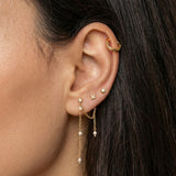 Close-up side profile of a woman’s ear wearing a layered gold ear stack, featuring a textured gold ear cuff on the upper cartilage, delicate gold stud earrings, and a fine gold chain drop earring accented with small pearls. The image clearly shows the soft movement of the chain, the contrast between polished gold and pearl details, and the placement across multiple piercings. Designed for women who enjoy elegant, feminine ear styling, this image helps customers visualise how to combine gold studs, cuffs, an