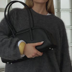 Woman styling the Lumi chunky butter yellow resin bangle with a grey oversized cashmere sweater and black leather handbag. A glossy statement resin bracelet designed for effortless everyday styling, capsule wardrobes, minimal fashion, Scandinavian-inspired outfits, and elevated neutral looks.