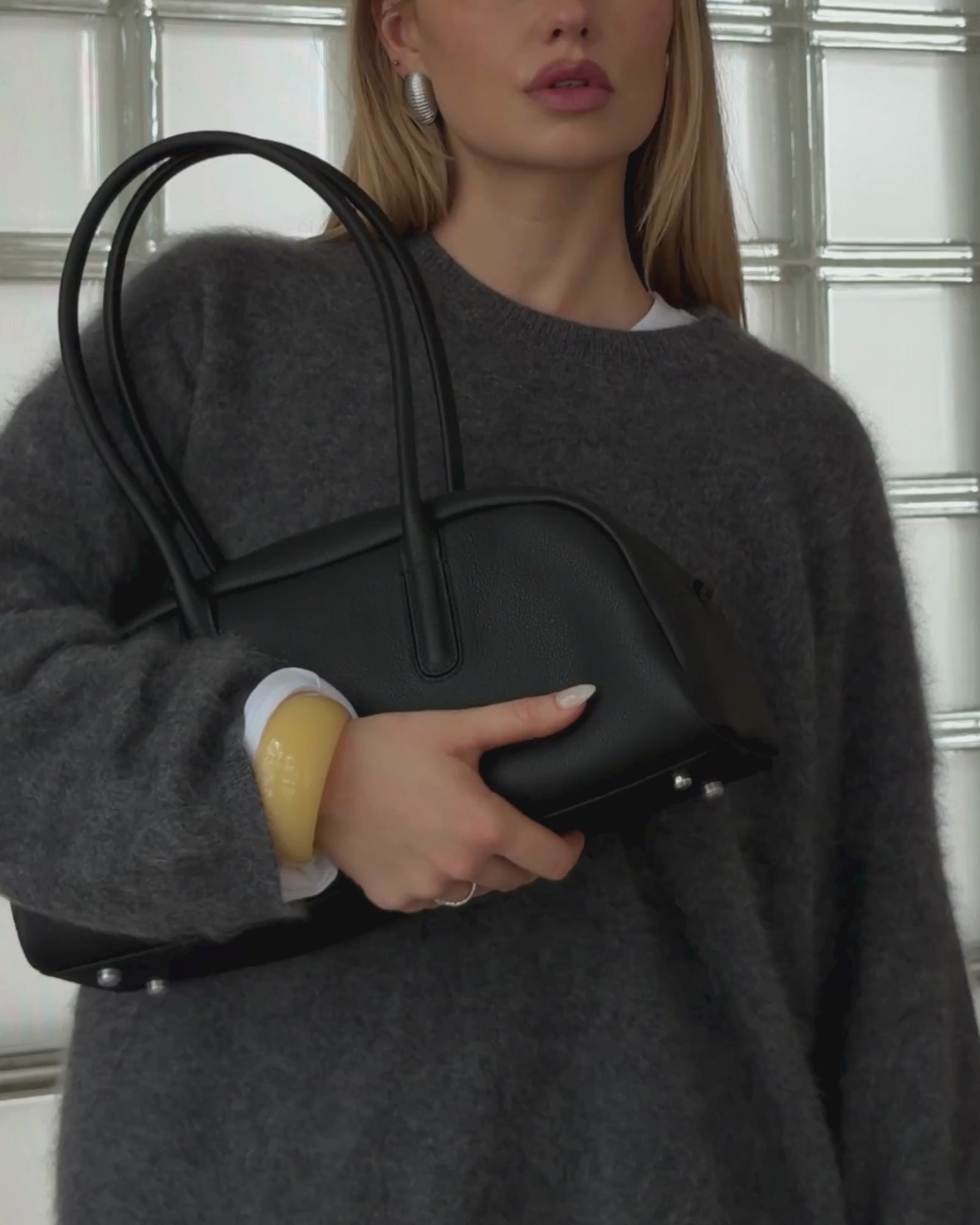 Woman styling the Lumi chunky butter yellow resin bangle with a grey oversized cashmere sweater and black leather handbag. A glossy statement resin bracelet designed for effortless everyday styling, capsule wardrobes, minimal fashion, Scandinavian-inspired outfits, and elevated neutral looks.